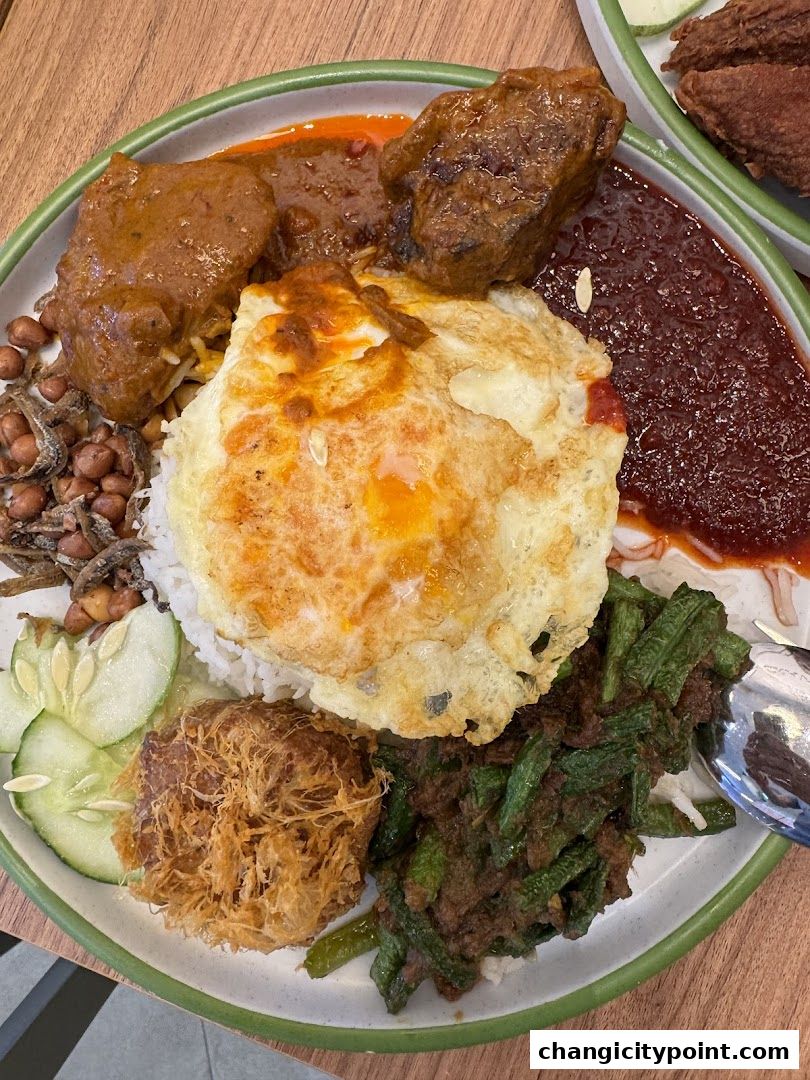 A delicious plate of Nasi Lemak with fried egg, chicken, sambal, and vegetables.
