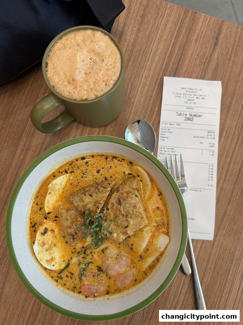 A bowl of Laksa Supreme with a cup of Teh Halia and a receipt.