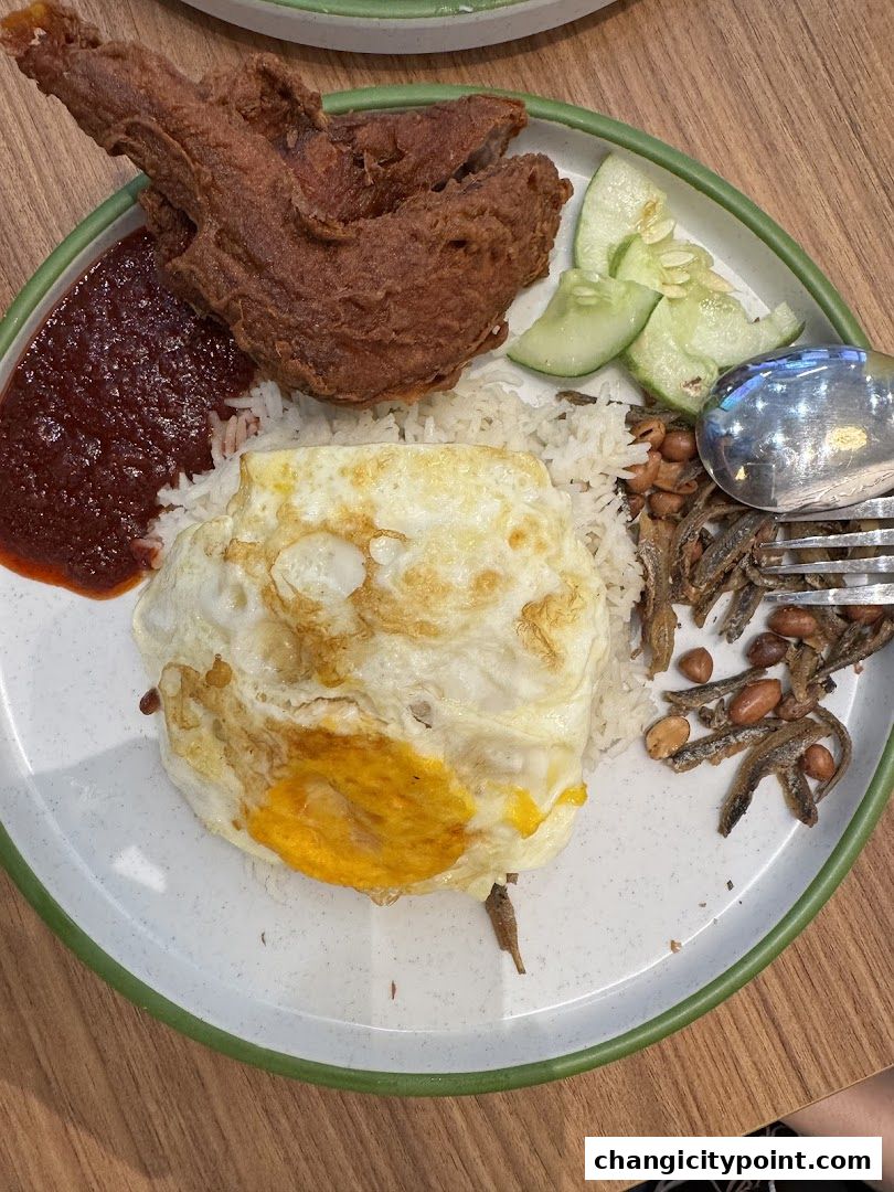 A plate of Nasi Lemak with fried chicken, fried egg, sambal, and anchovies.