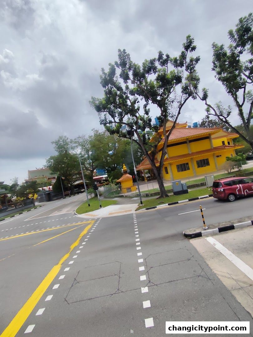 A bright yellow building with an orange roof is visible behind trees and a road.