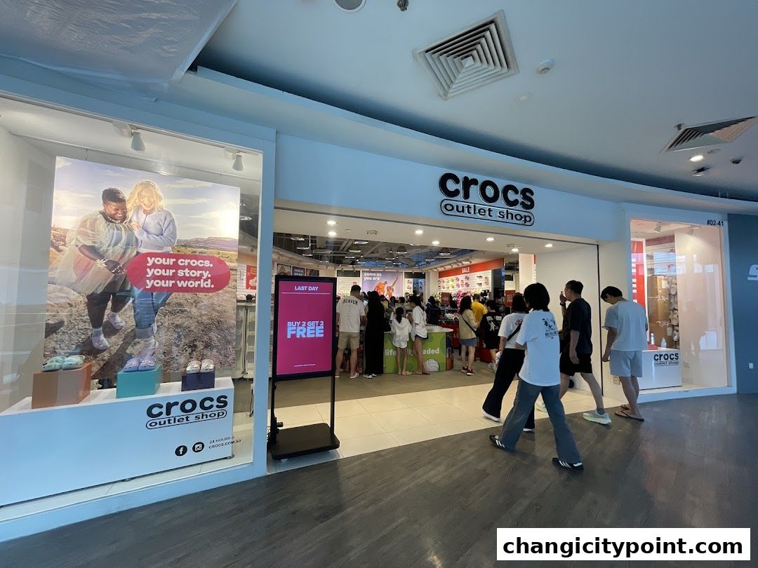 The exterior of a Crocs Outlet shop with a large advertisement and people entering.