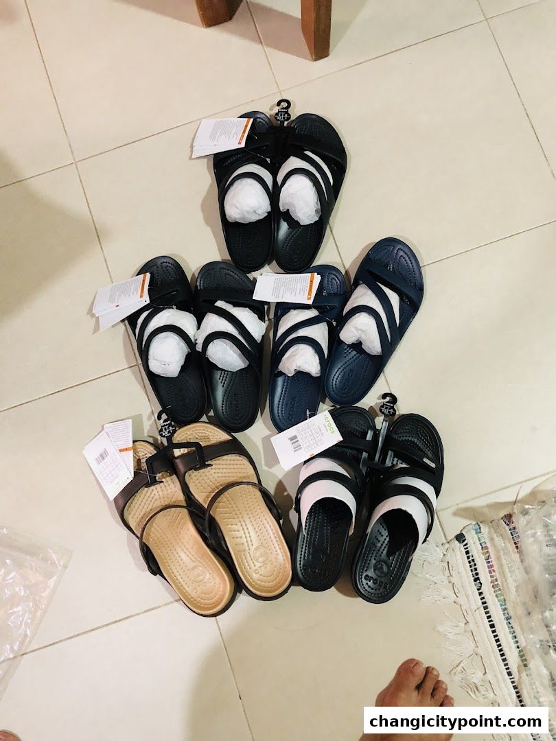 A collection of Crocs sandals and slides are displayed on a tiled floor.