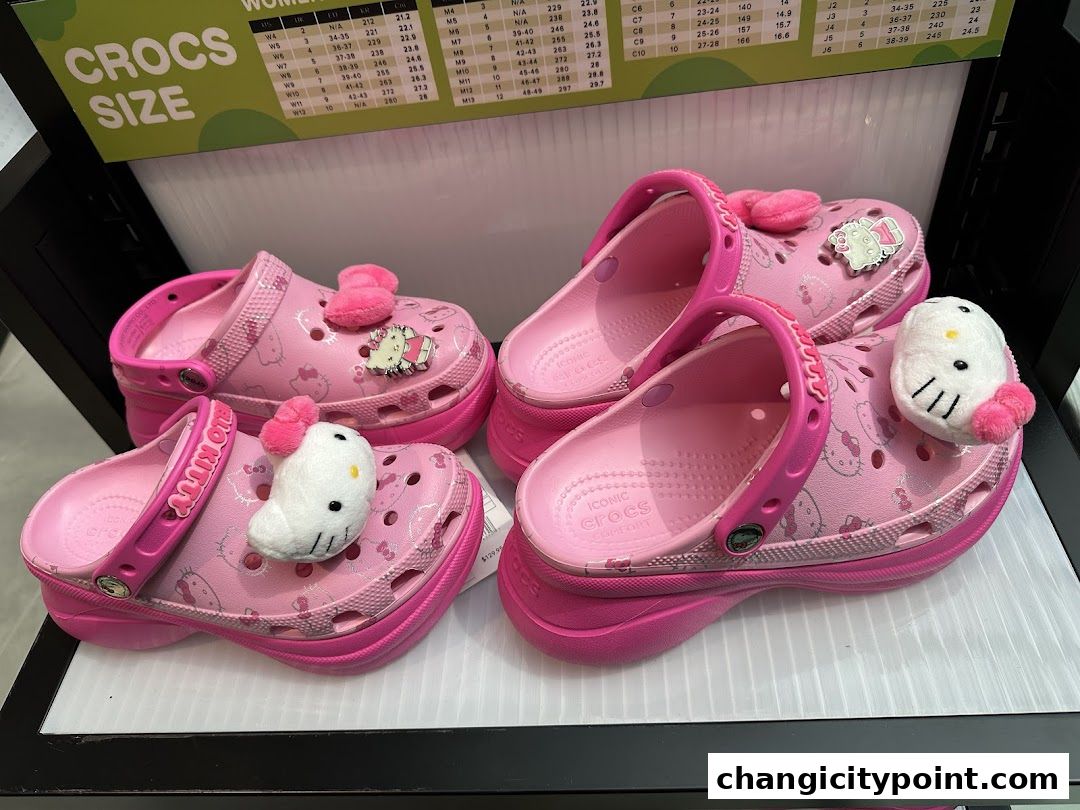 Pink Hello Kitty Crocs with fluffy charms and a size chart in the background.