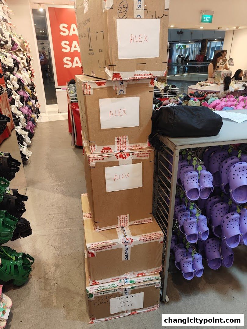 Stack of boxes labeled 'ALEX' and rows of colorful Crocs shoes on display.