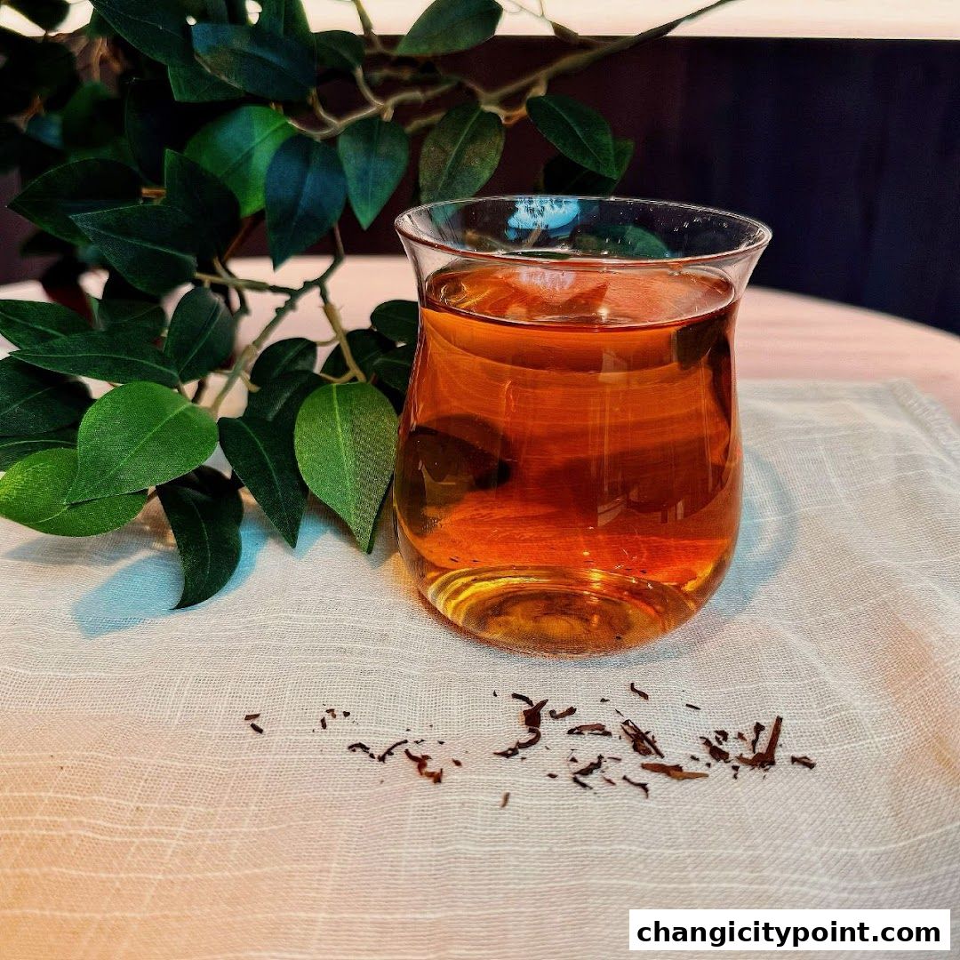 A glass of amber-colored tea sits next to green leaves and scattered tea leaves.