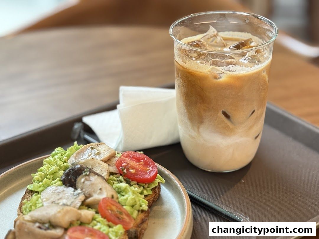 A close-up of avocado toast with mushrooms and tomatoes, next to an iced coffee.