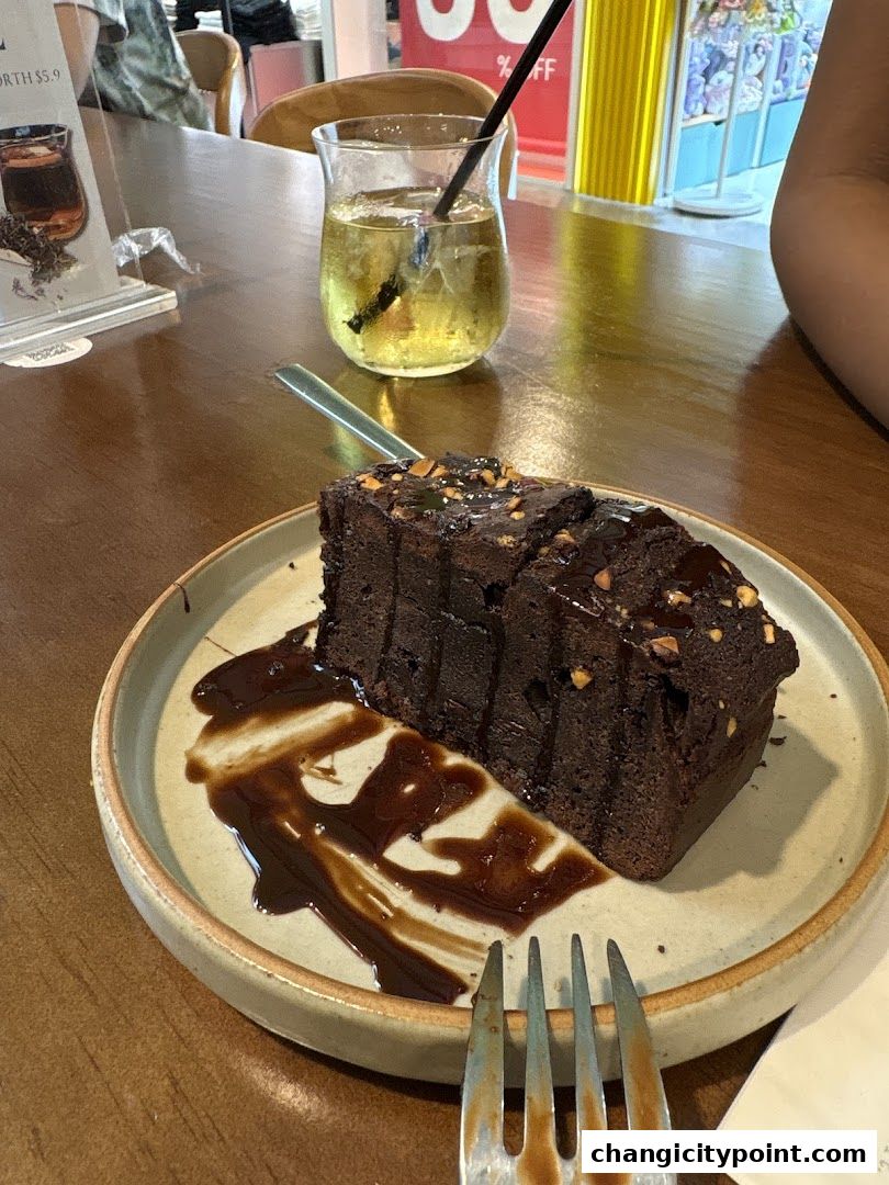 A slice of rich chocolate cake with nuts and chocolate sauce, served with a refreshing drink.