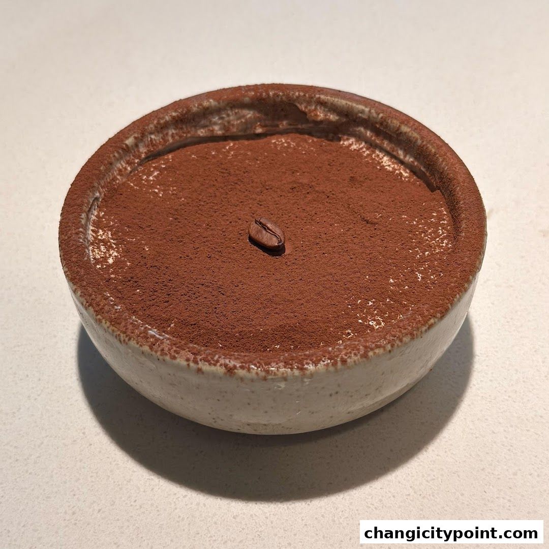 A close-up of a tiramisu dessert in a rustic bowl, dusted with cocoa powder and a coffee bean.