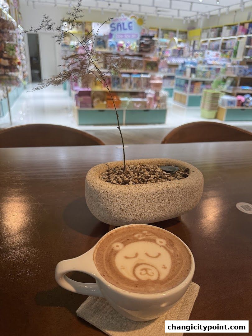 A latte with bear art sits on a table in front of a shop with shelves of products.