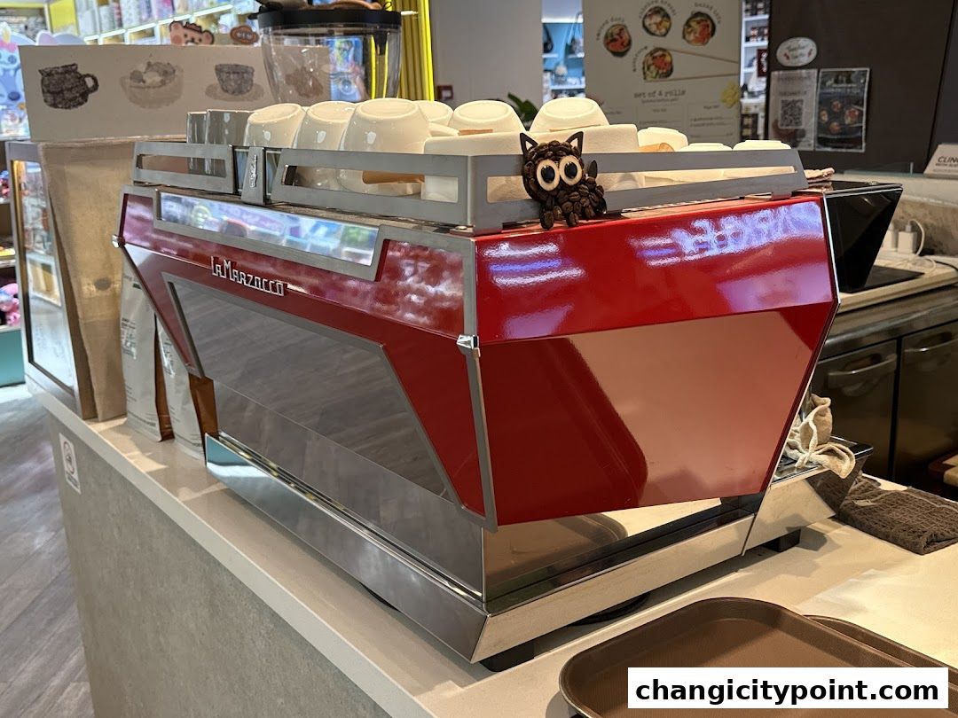 A bright red La Marzocco espresso machine with cups on top and a cute owl decoration.
