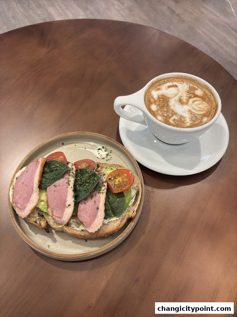 A delicious avocado toast with duck and a latte with latte art on a wooden table.