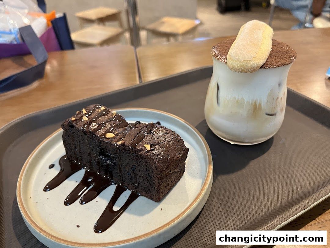 A rich chocolate brownie and a coffee drink topped with a biscuit on a tray.
