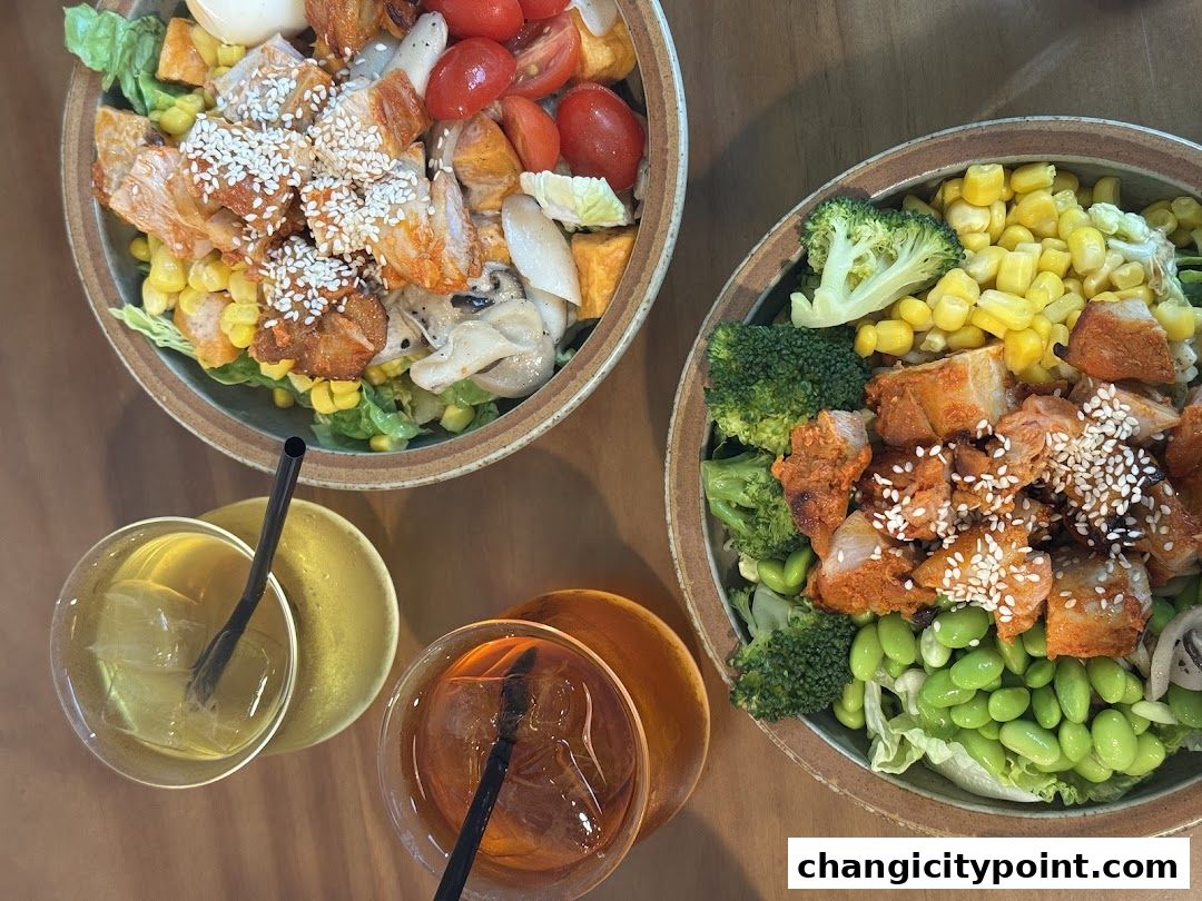 Two healthy and colorful salads with chicken, corn, broccoli, edamame, and tomatoes, served with drinks.