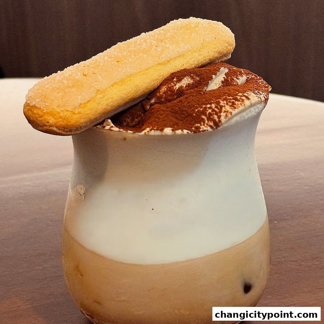 A delicious tiramisu dessert in a glass with a ladyfinger on top.