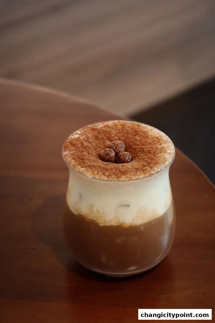 A close-up of a creamy iced coffee topped with cocoa powder and crunchy toppings.