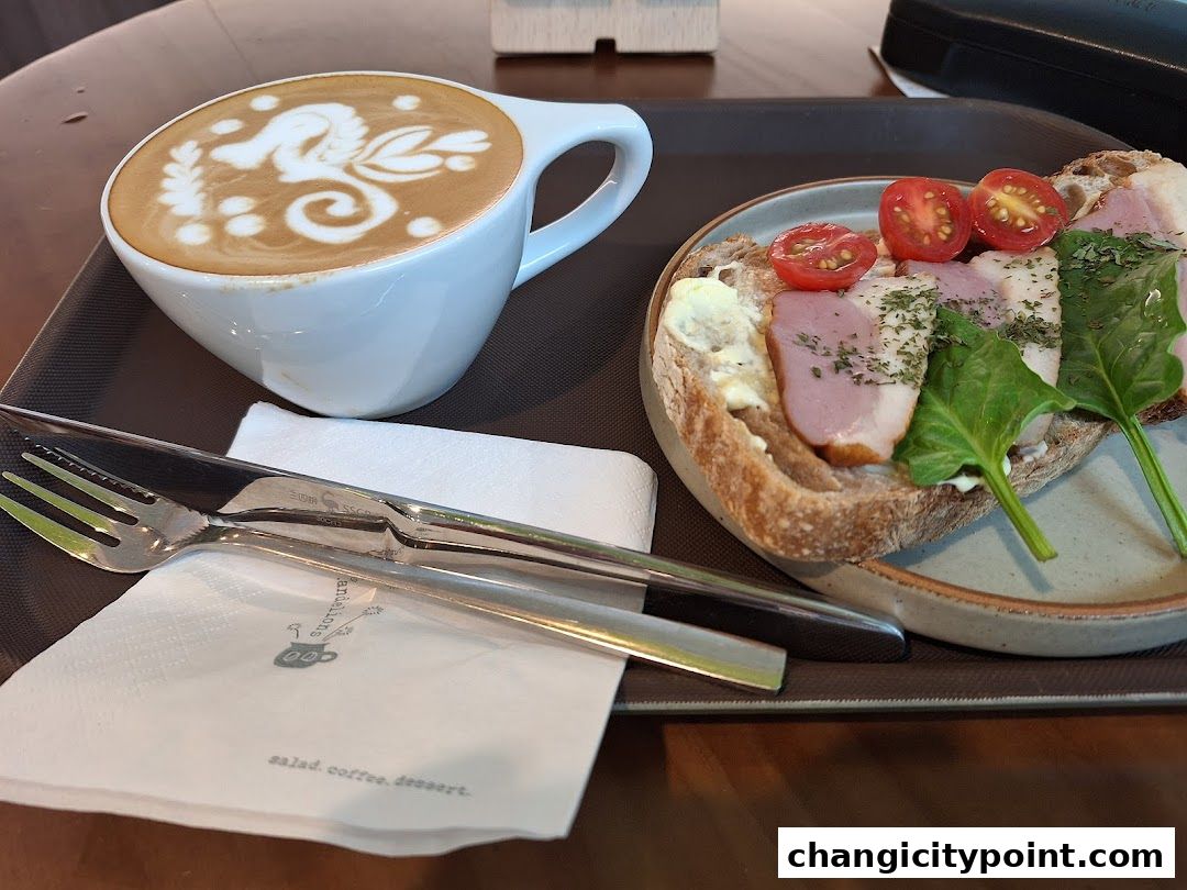 A latte with art and a sandwich with tomatoes and meat on a tray.