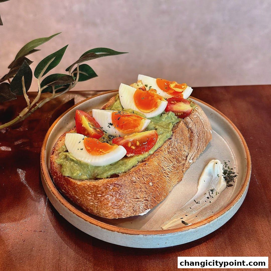 Avocado toast with boiled eggs and tomatoes on a rustic bread slice.