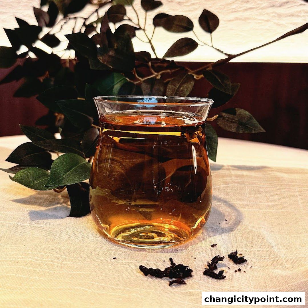 A glass of amber-colored tea sits on a white tablecloth with loose tea leaves nearby.