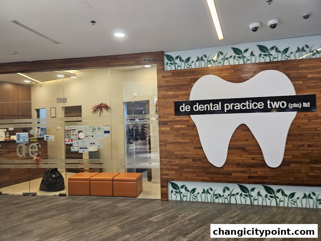 The exterior of De Dental Practice Two Ltd, featuring a modern glass entrance and a large tooth logo.