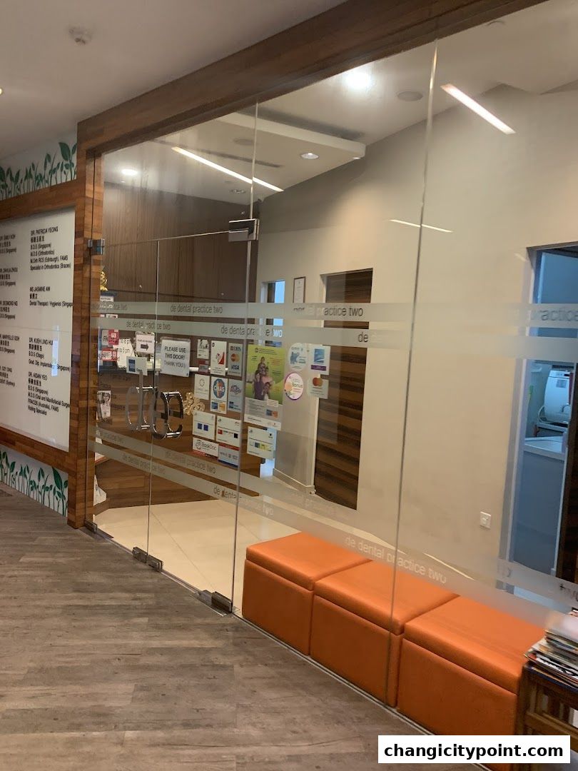 Entrance to De Dental Practice Two Ltd with glass doors and an orange waiting bench.