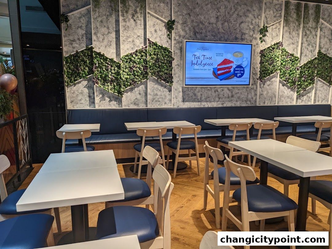 Interior of Delifrance cafe with tables, chairs, and a digital menu display.