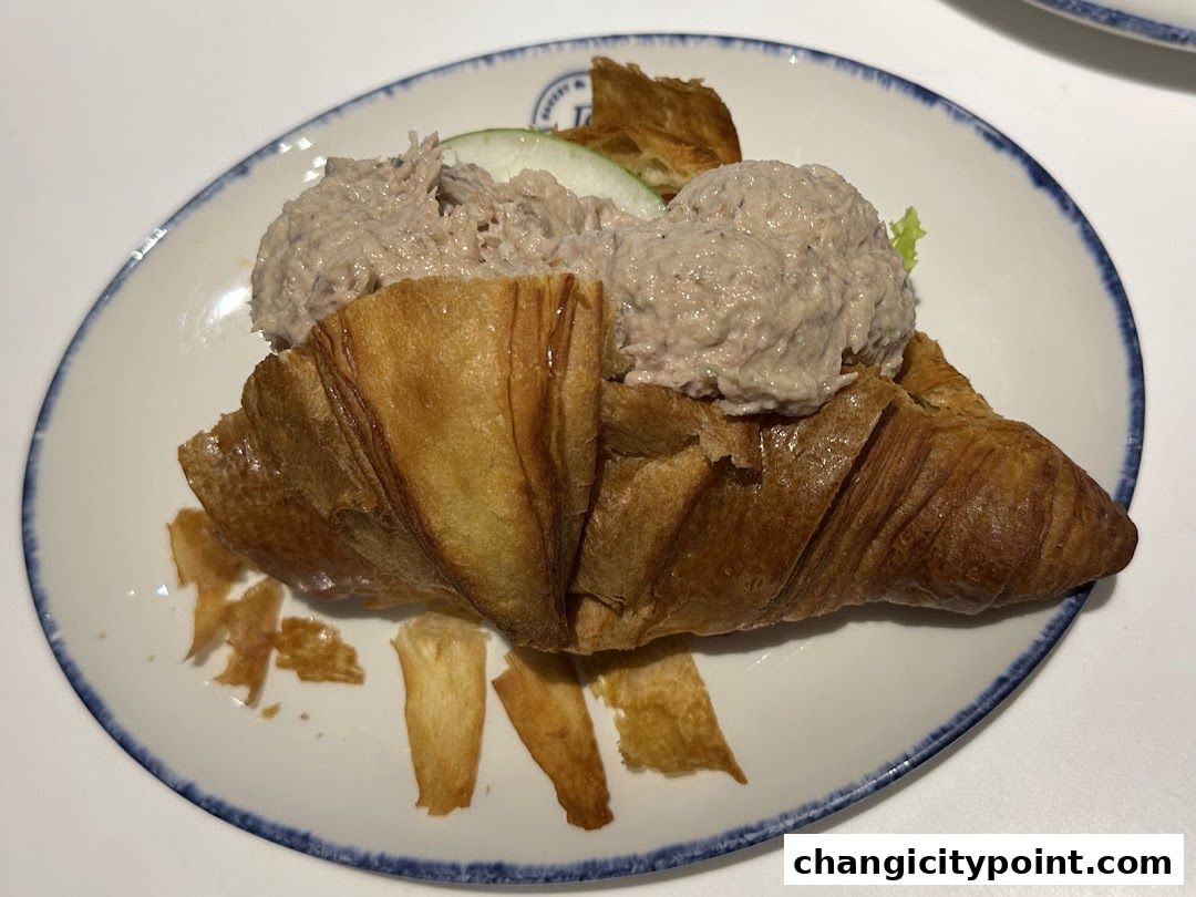 A delicious tuna croissant sandwich served on a white plate with a blue rim.