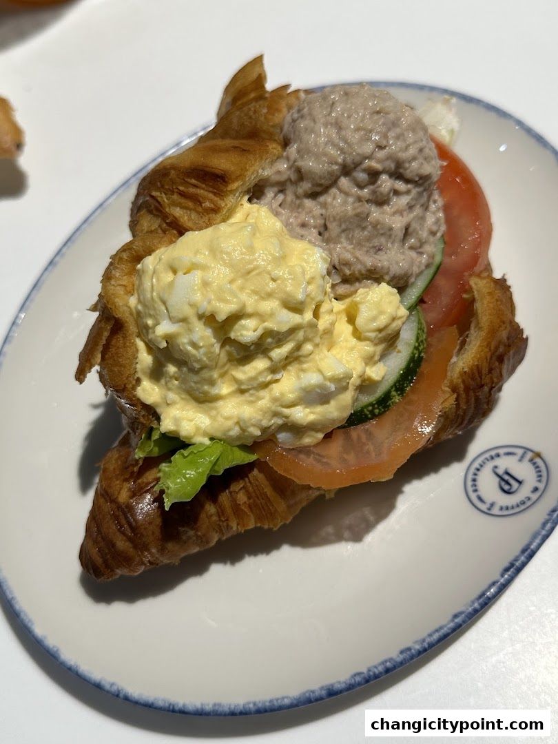 A delicious croissant sandwich filled with tuna salad, egg salad, salmon, and vegetables.