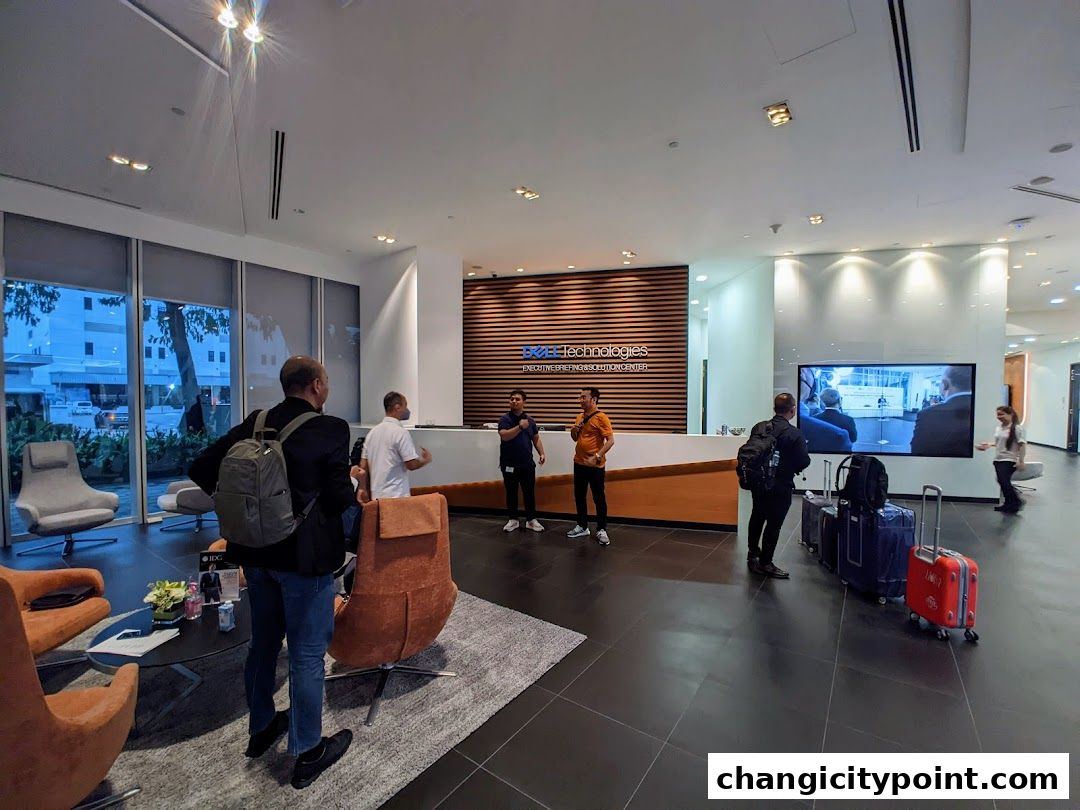 Interior of a modern office lobby with people and luggage near a reception desk.
