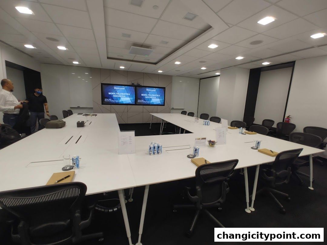 A modern conference room with a large U-shaped table and two screens displaying a welcome message.