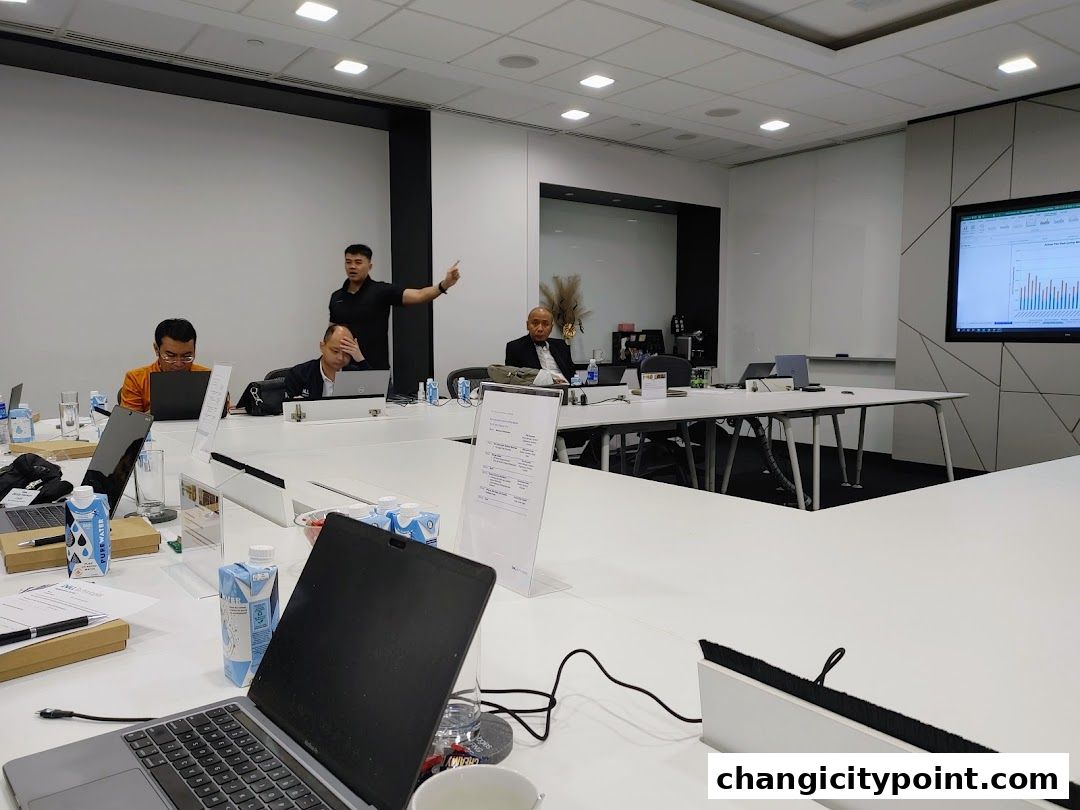 A meeting in progress with people working on laptops and a presentation on a screen.