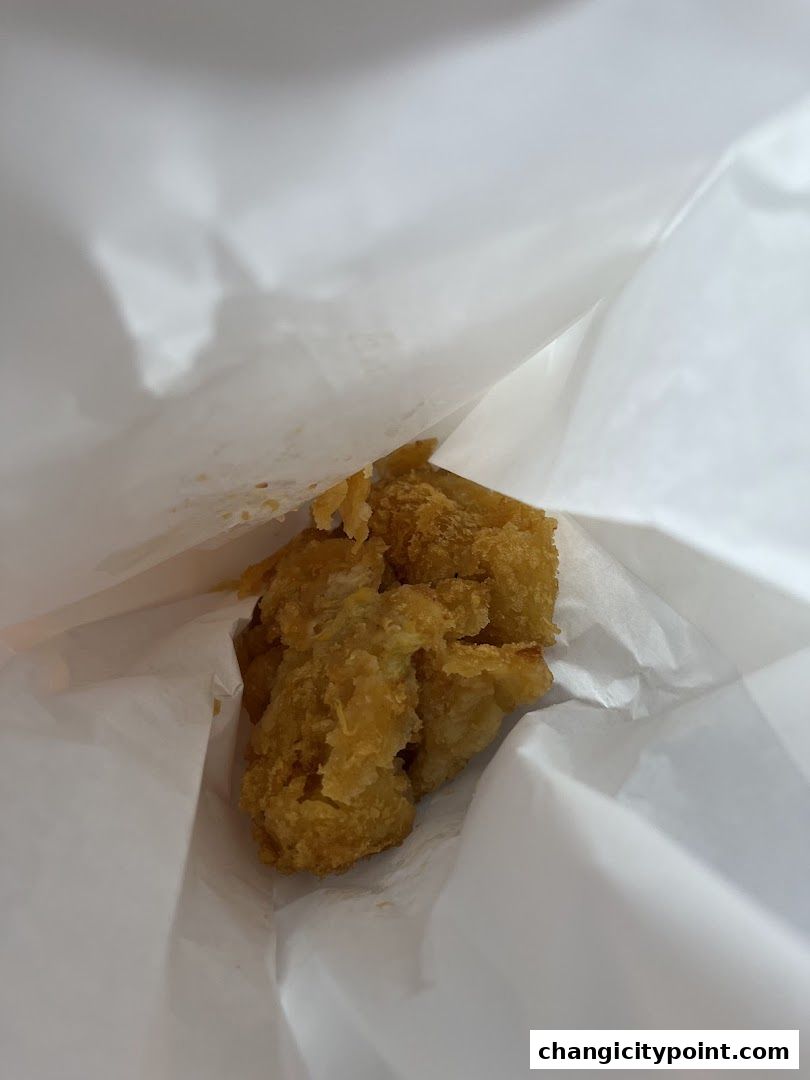Crispy fried chicken pieces are presented in a white paper bag.