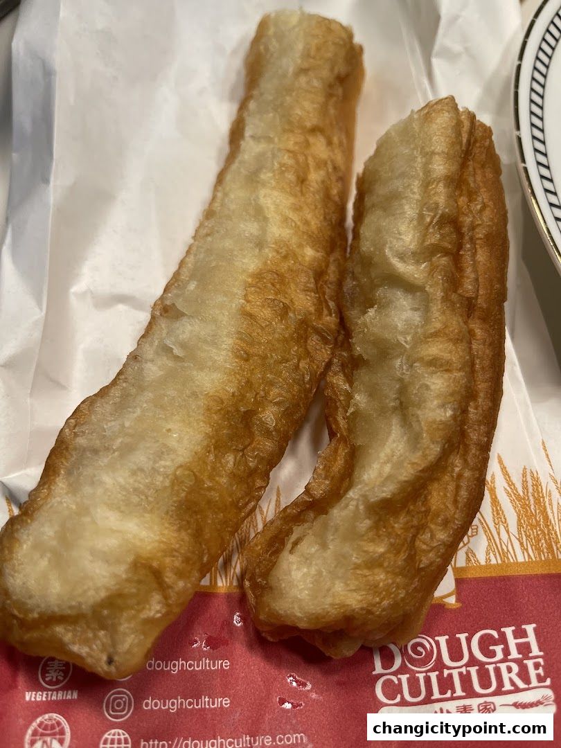Two golden-brown fried dough sticks served on white paper with the Dough Culture logo.