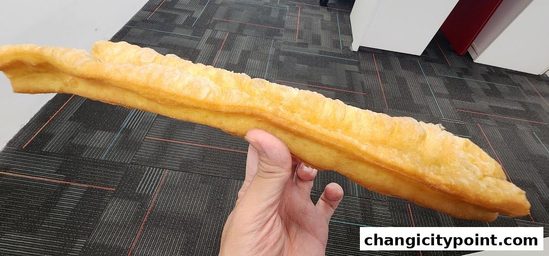 A hand holds a long, golden-brown fried dough stick, likely from Dough Culture.