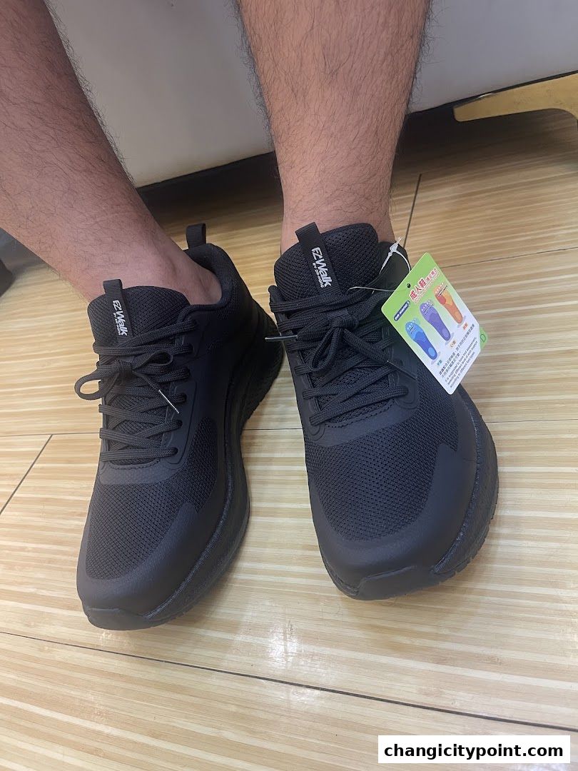 A person wearing black EZ-Walk sneakers with a product tag attached.