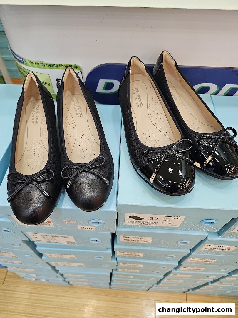Two pairs of black ballet flats with bows displayed on shoe boxes.