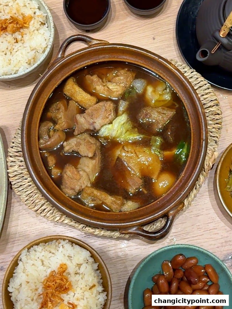 A steaming pot of Bak Kut Teh with rice and side dishes.