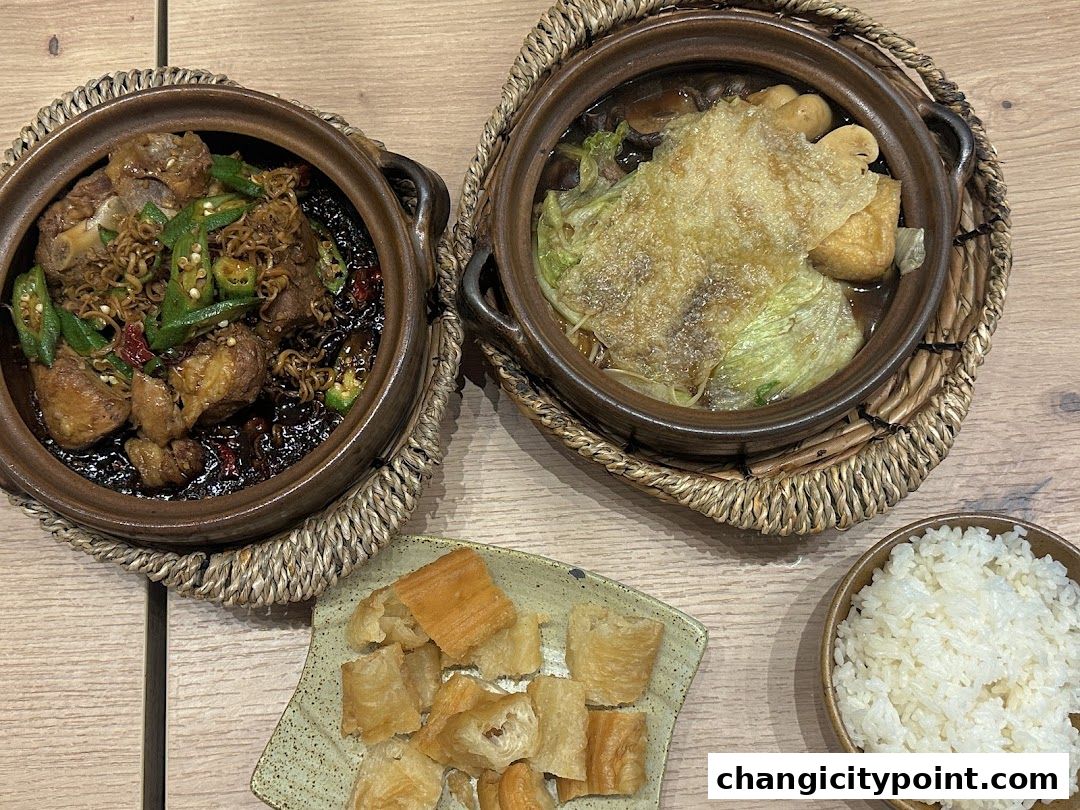 Two clay pots of Bak Kut Teh, fried dough sticks, and a bowl of rice on a wooden table.