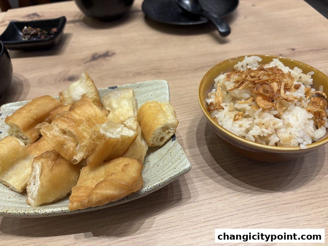 A bowl of rice topped with fried shallots and a plate of fried dough sticks.