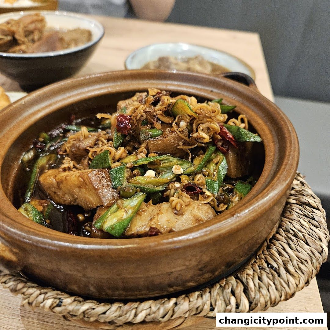 A close-up of a clay pot filled with braised pork belly, okra, and noodles.