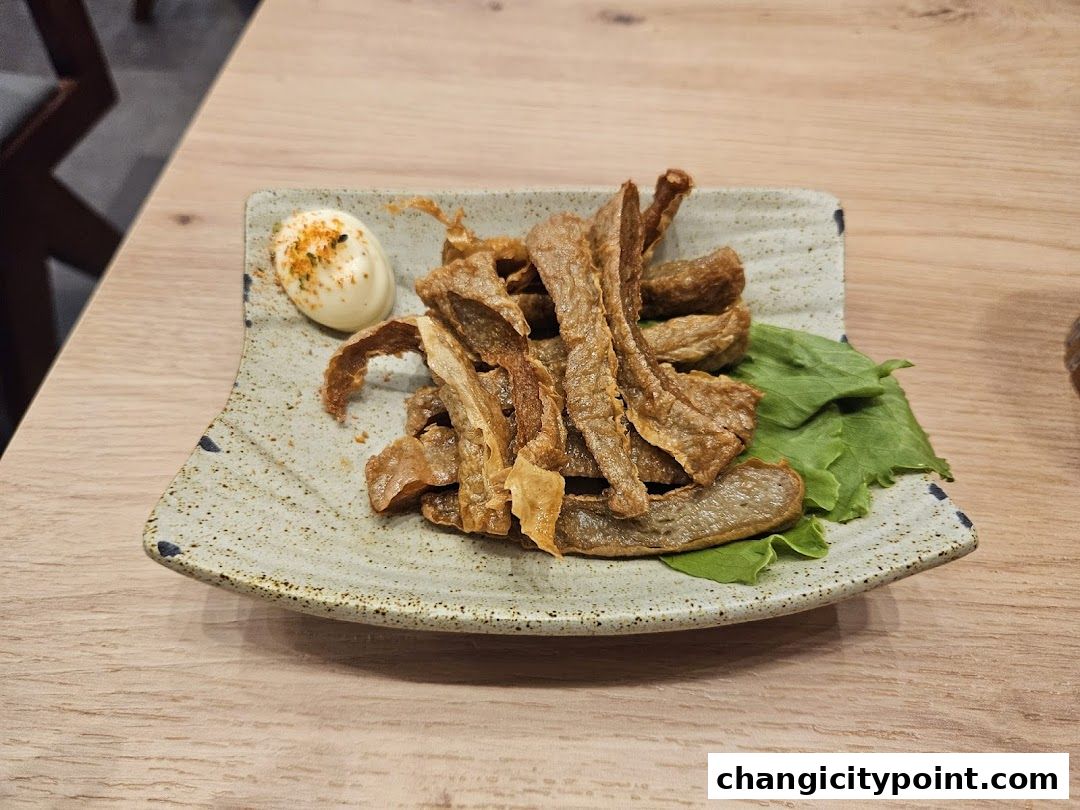 A plate of crispy fried pork belly with a dollop of mayonnaise and a lettuce leaf.