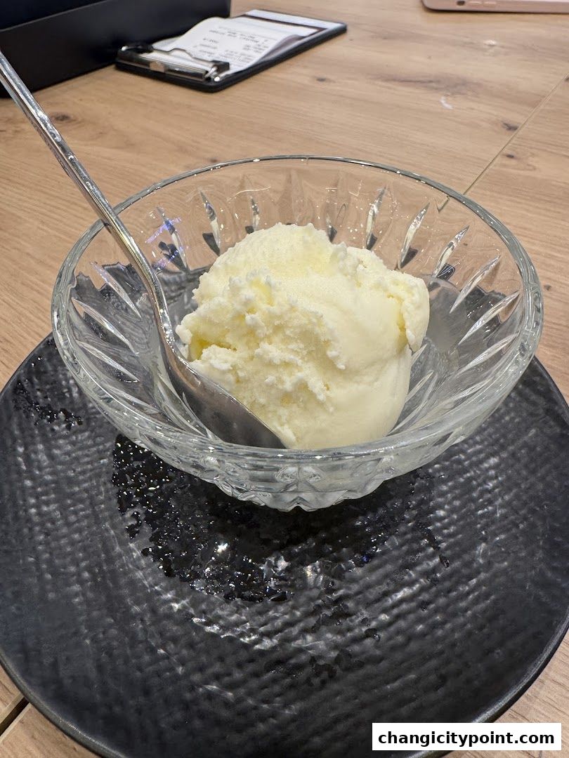 A scoop of creamy ice cream served in a crystal bowl on a black plate.