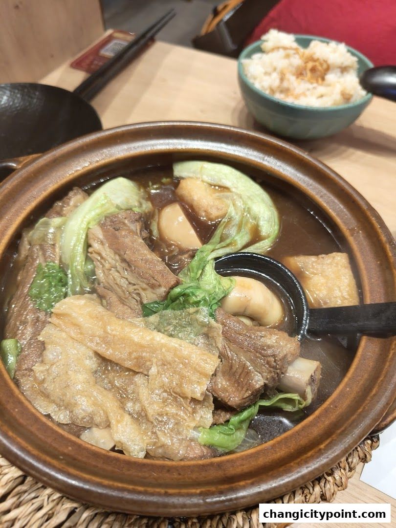 A steaming bowl of Bak Kut Teh with tender pork ribs, vegetables, and fried tofu skin.