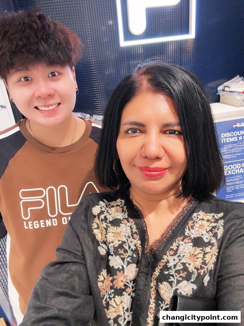 Two people smiling in front of a FILA outlet store with a discount sign.