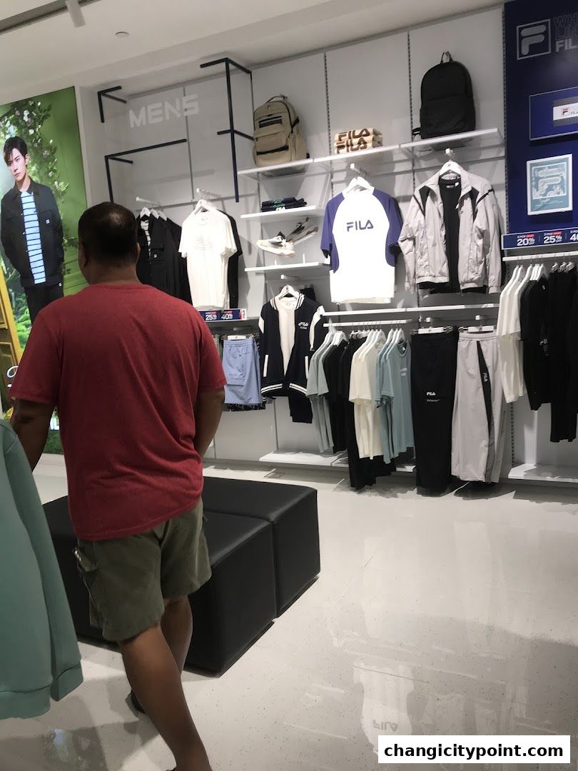 A man walks through a FILA outlet store displaying men's apparel and accessories.