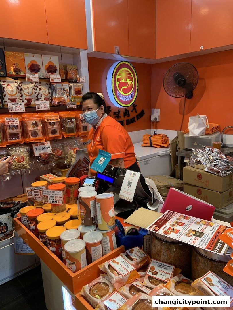 A shopkeeper stands behind a counter filled with various packaged meat products and snacks.