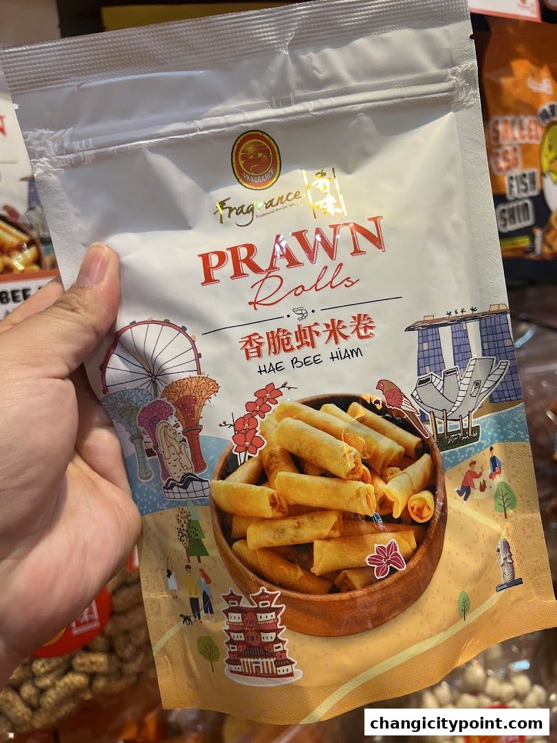 A hand holds a bag of Fragrance Prawn Rolls with a traditional Singaporean skyline illustration.