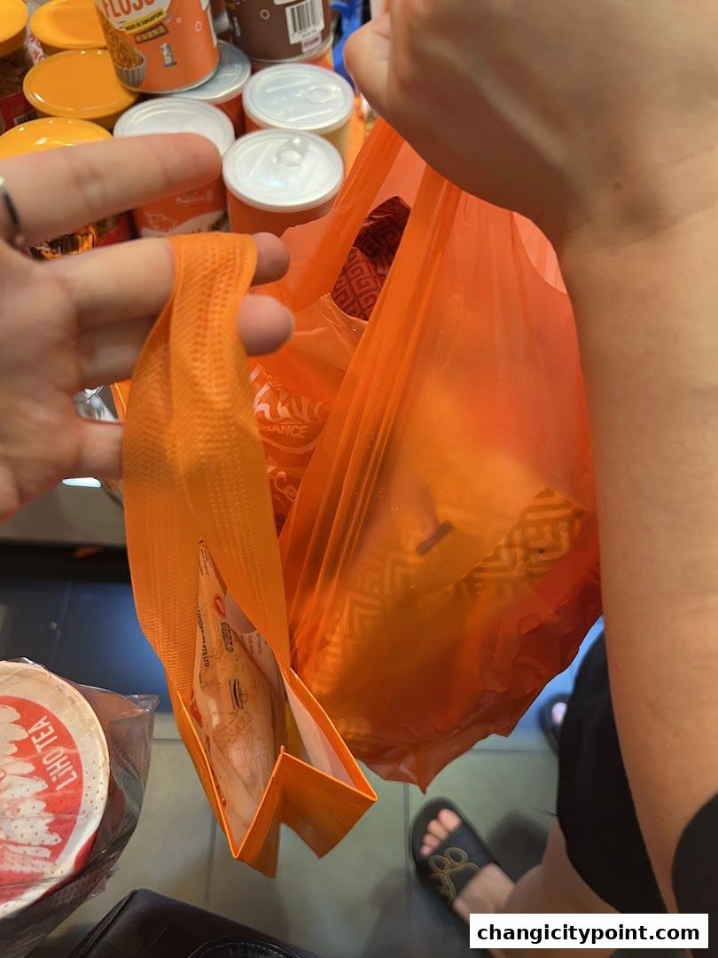 Hands holding an orange shopping bag filled with products from Fragrance Bak Kwa.