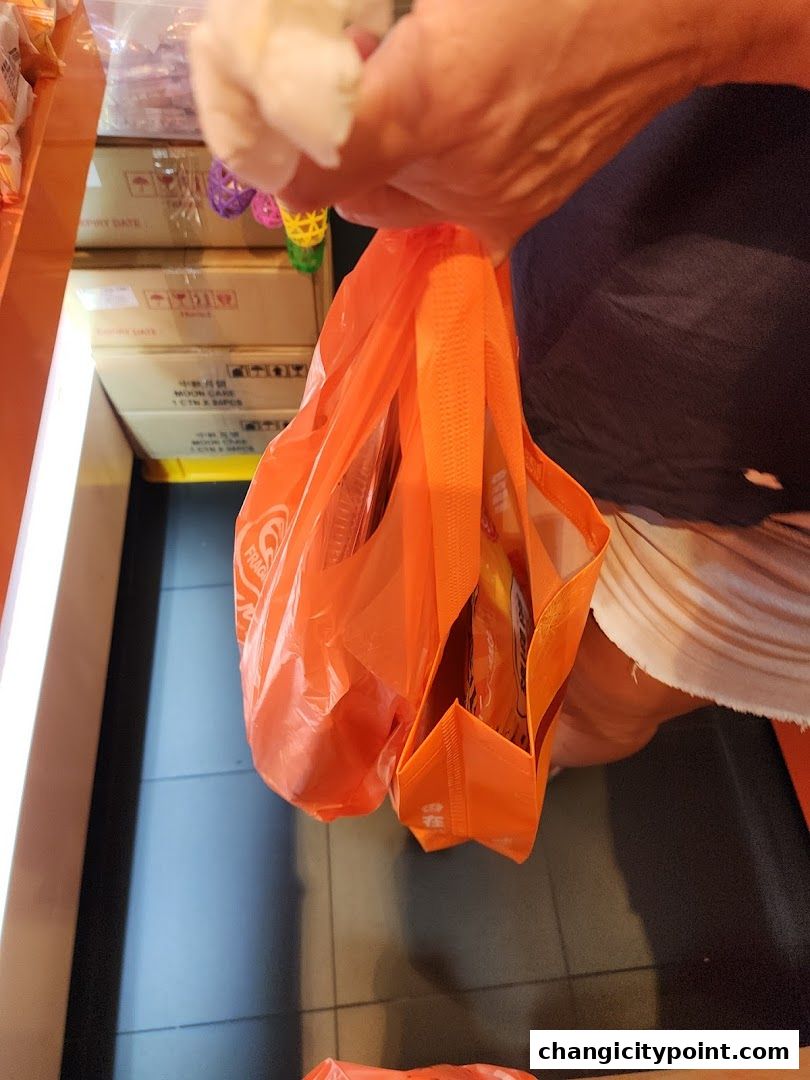 A person holds an orange shopping bag filled with items from Fragrance Bak Kwa.