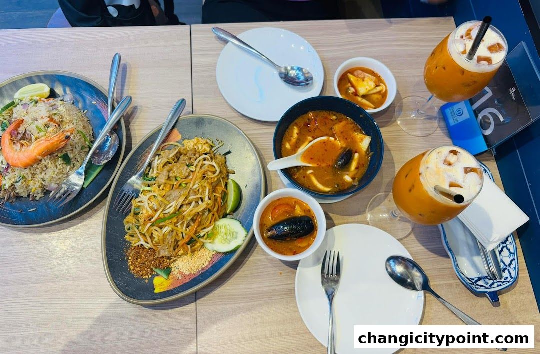 A table laden with Thai dishes including Pad Thai, fried rice, soup, and iced tea.