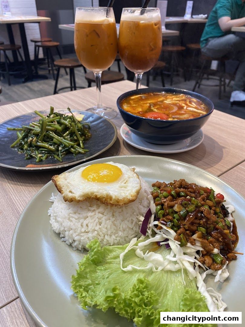 A table laden with Thai food, including rice, stir-fried vegetables, soup, and iced tea.